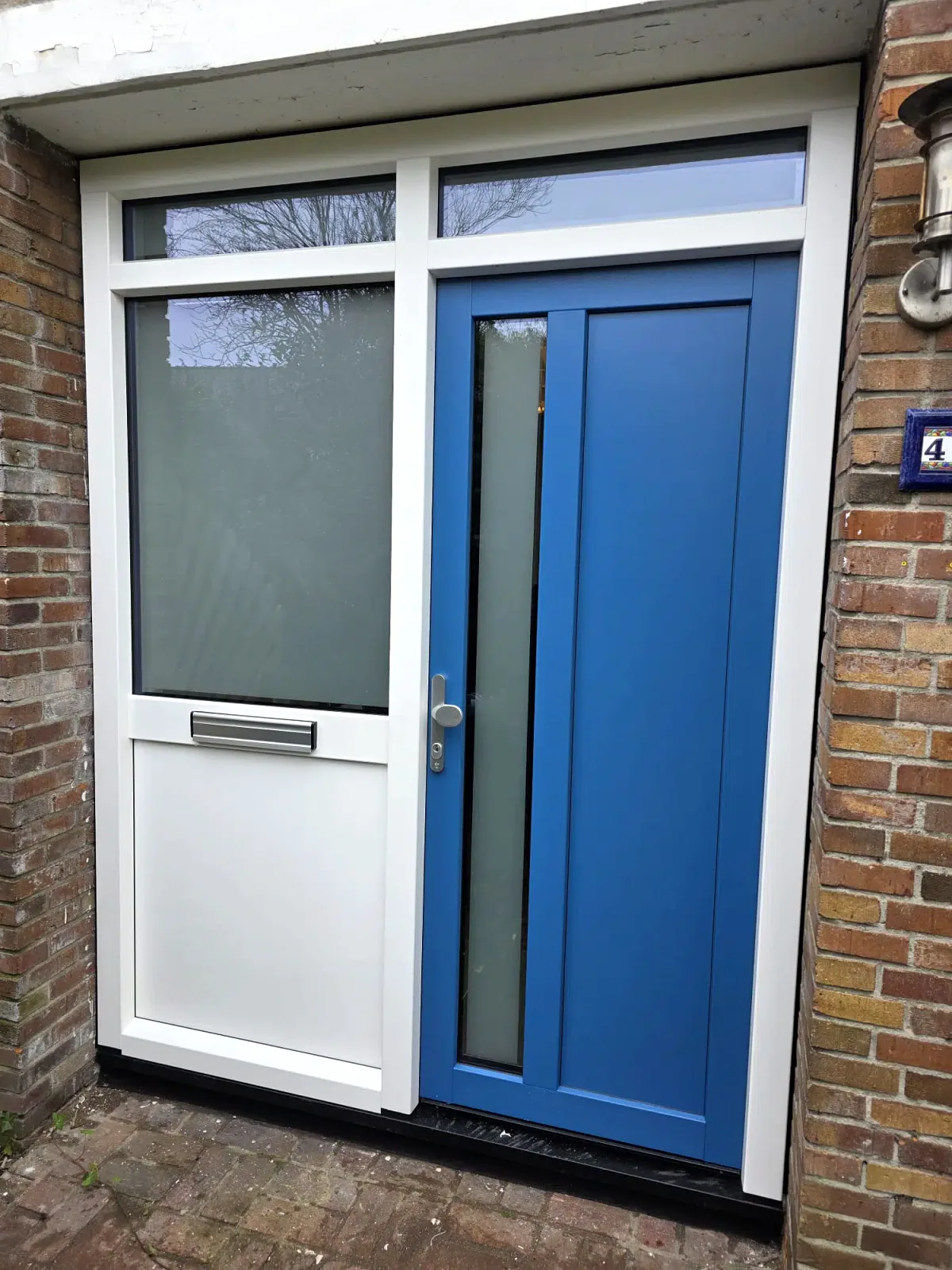 Blauwe kunststof voordeur met wit kader en zijlicht in een bakstenen gevel